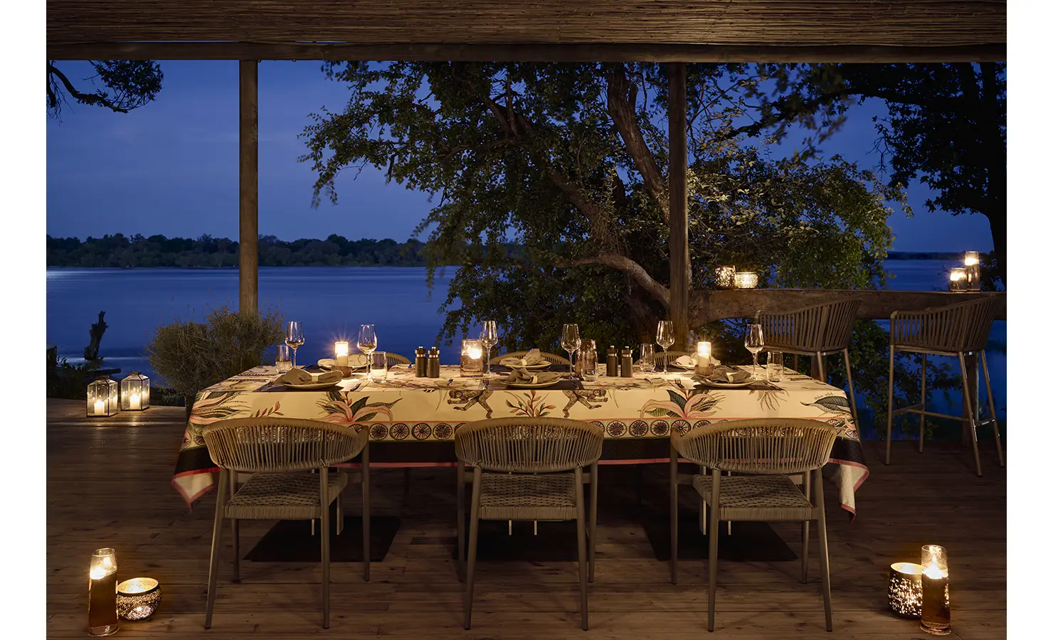 Perfect Hideaways: Candlelit dinner on the deck at night, table dressed in patterned cloth with lanterns and the river beyond. Hippo Creek Villa, Zambezi National Park.