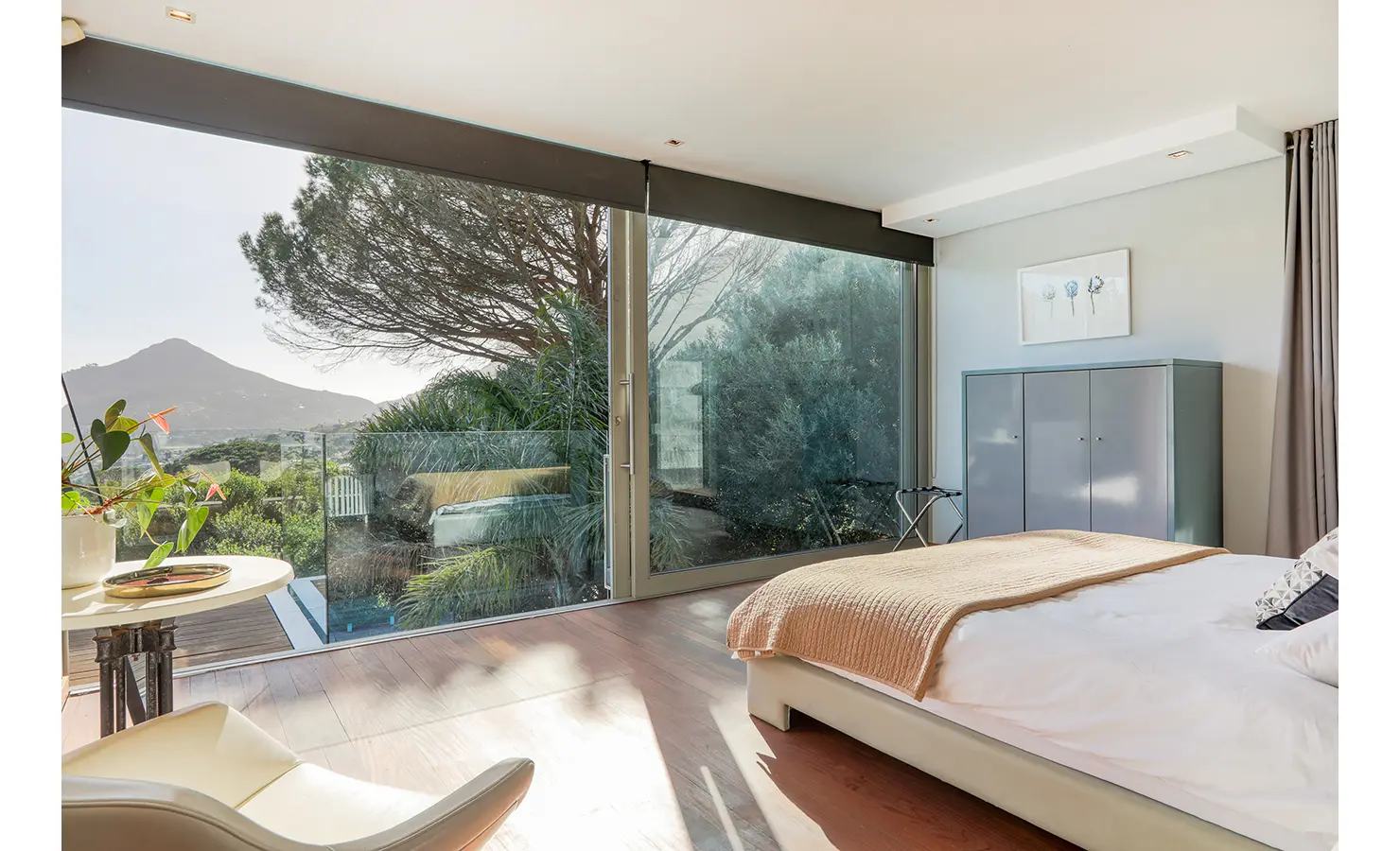 Perfect Hideaways: Serene bedroom with a wall of glass framing the mountain and treetops, pared‑back furnishings and warm timber floors, Spa House, Hout Bay