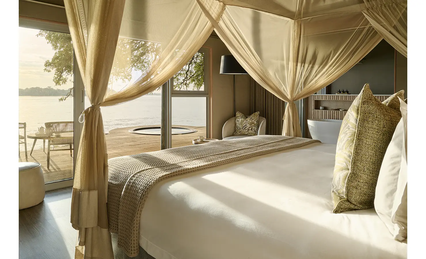 Perfect Hideaways: Elegant bedroom with canopy-draped bed, neutral linens and direct deck access to a private plunge pool beside the river. Hippo Creek Villa, Zambezi National Park.