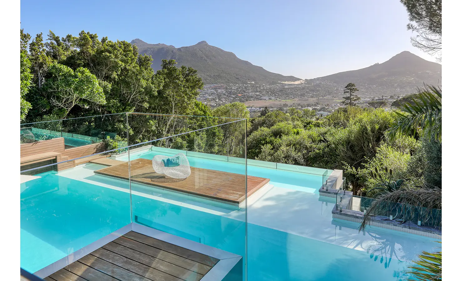 Perfect Hideaways: Elevated view over tiered infinity pool with frameless glass balustrade, timber island daybed and mountain panorama, Spa House, Hout Bay