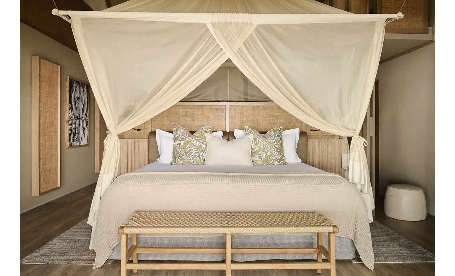 Perfect Hideaways: Serene bedroom with neutral tones, canopy bed and rattan bench, styled with botanical prints and woven textures. Hippo Creek Villa, Zambezi National Park.