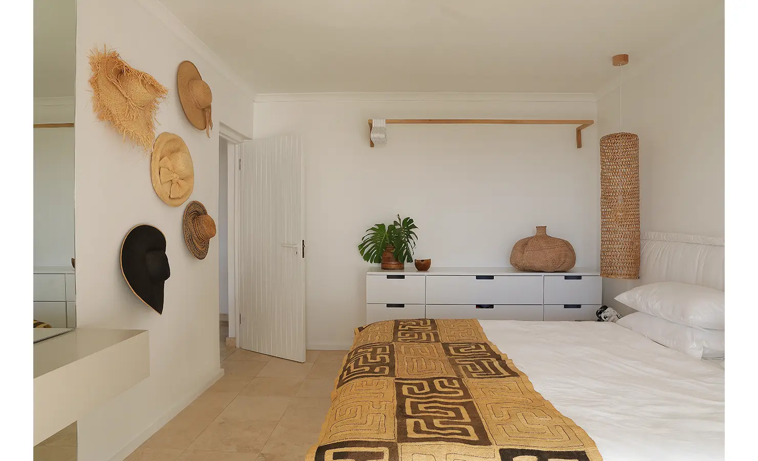 Perfect Hideaways: light guest bedroom with sun hats displayed on the wall, sleek white cabinetry and a bed layered with a patterned ochre throw, Blanc de Blanc, Yzerfontein