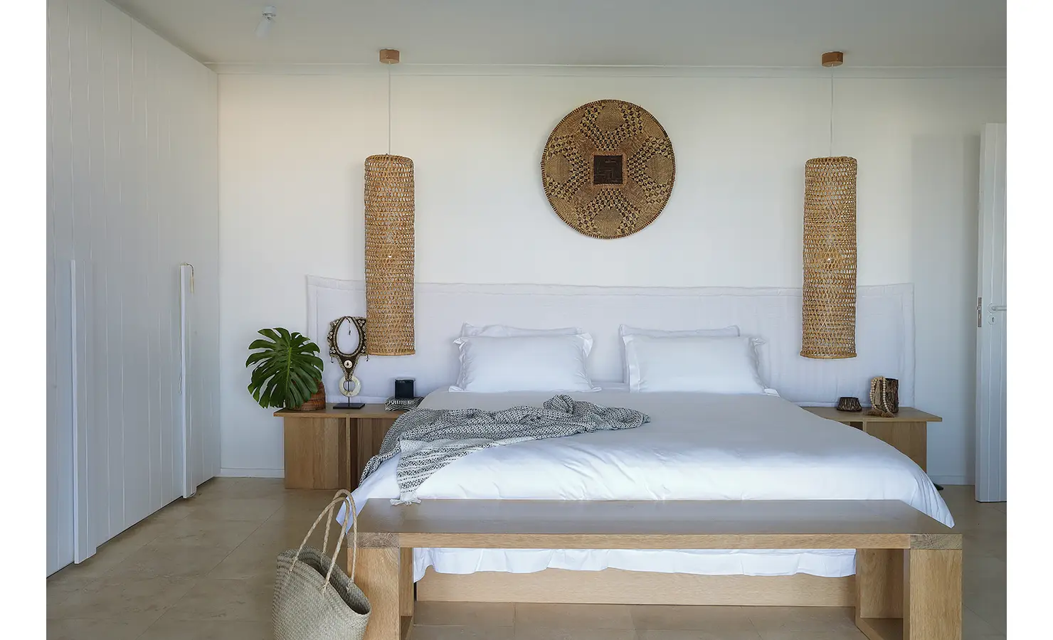 Perfect Hideaways: tranquil main bedroom with white linen, long woven pendant lights, circular basket wall art and timber bench, with leafy monstera accents, Blanc de Blanc, Yzerfontein