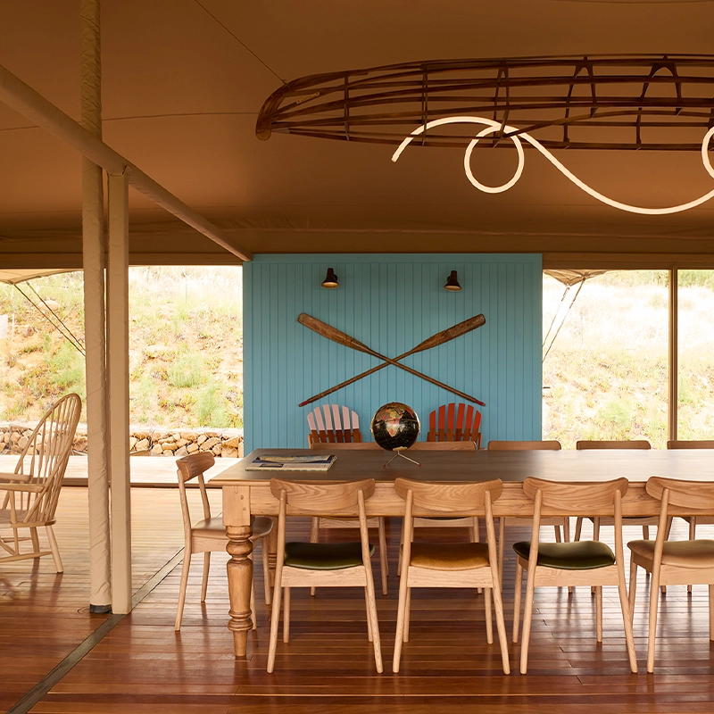 Perfect Hideaways: Open-plan camp dining under canvas with long wooden table, canoe-frame light and a blue panel with crossed oars, Franschhoek, Camp Canoe