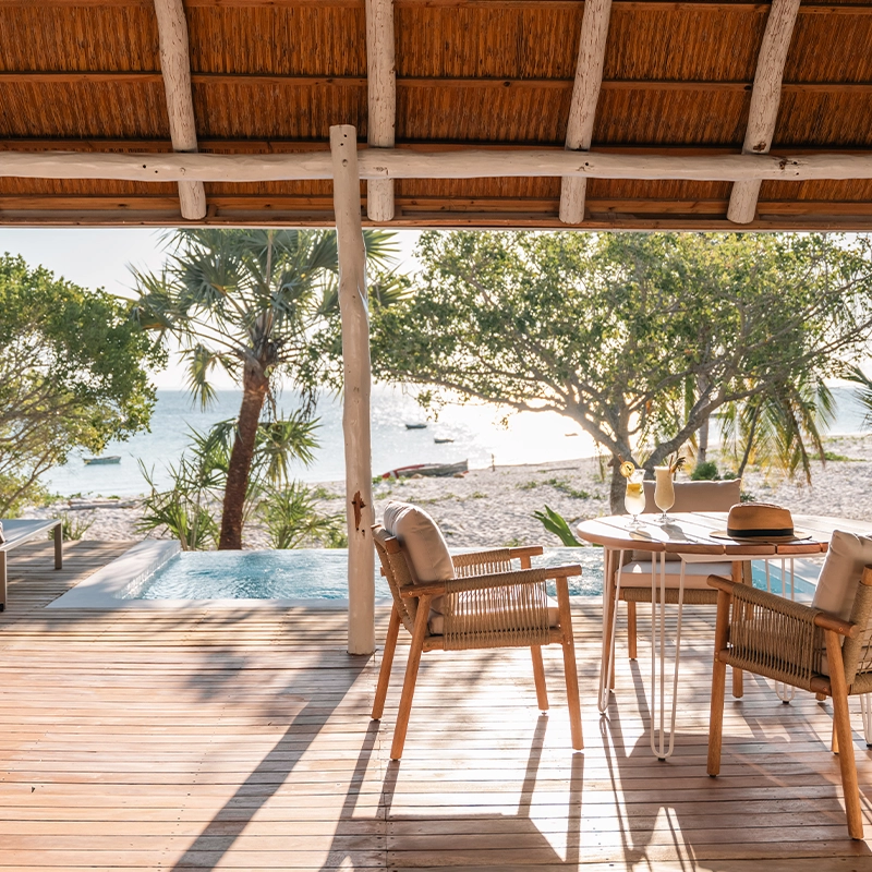 Perfect Hideaways: Shaded timber deck beneath a thatched roof with woven chairs and breakfast set-up, sun loungers and a private plunge pool overlooking palm-fringed white sand and the Indian Ocean, Benguerra Island, Azura Marlin Beach