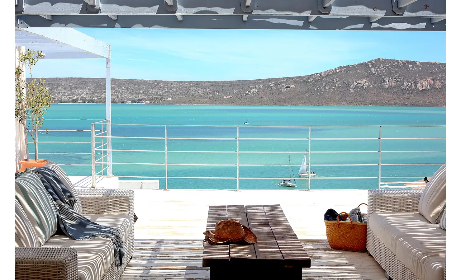 Perfect Hideaways: sun-drenched deck with wicker sofas, slatted pergola and coffee table, overlooking sailboats on a turquoise lagoon and rugged hills, Langebaan, Lagoon Lookout.