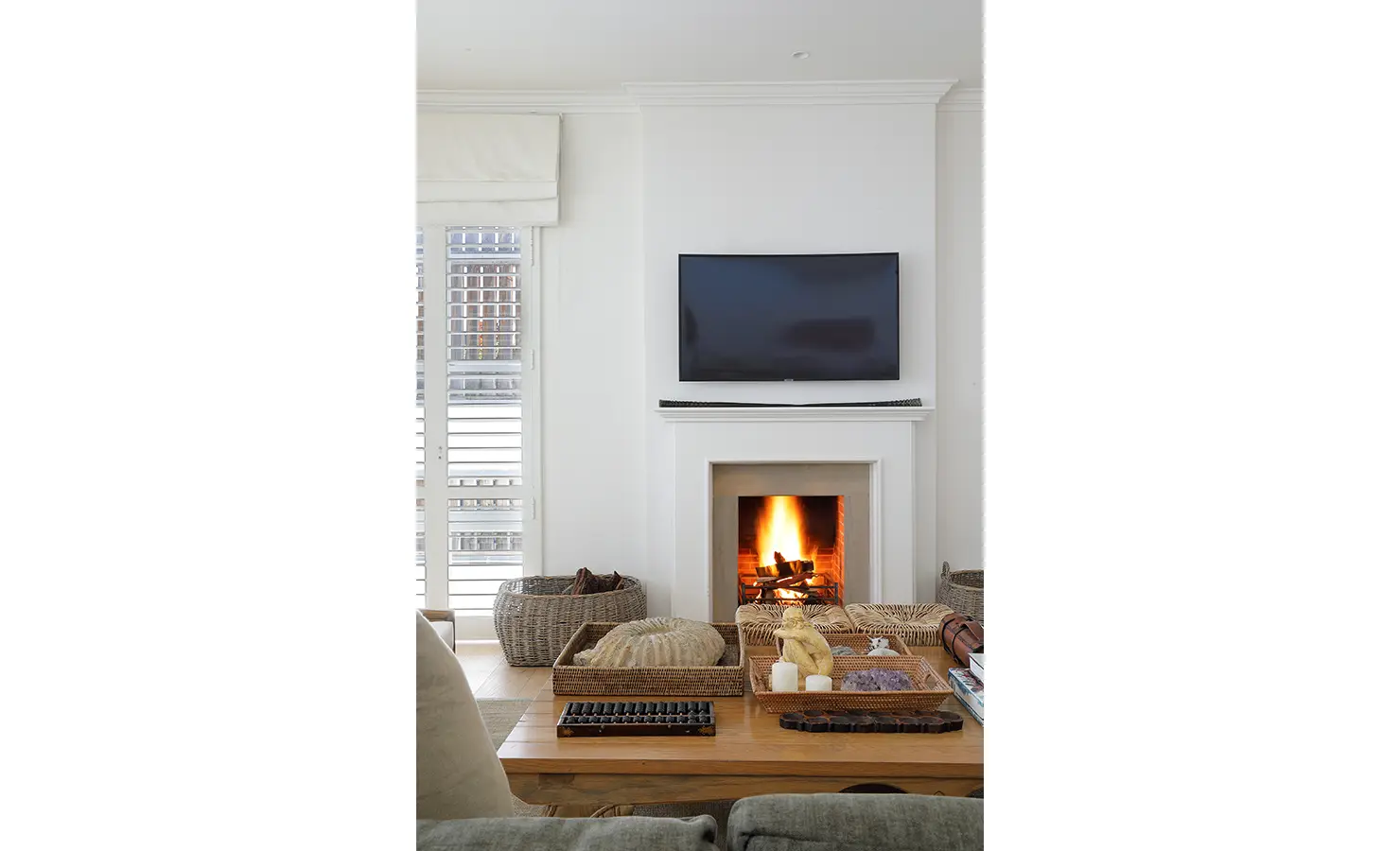 Perfect Hideaways: A close-up of a glowing fireplace beneath a mounted TV, surrounded by textured baskets and decorative trays filled with shells and books for a collected, cosy aesthetic. Fresnaye, The Townhouse.