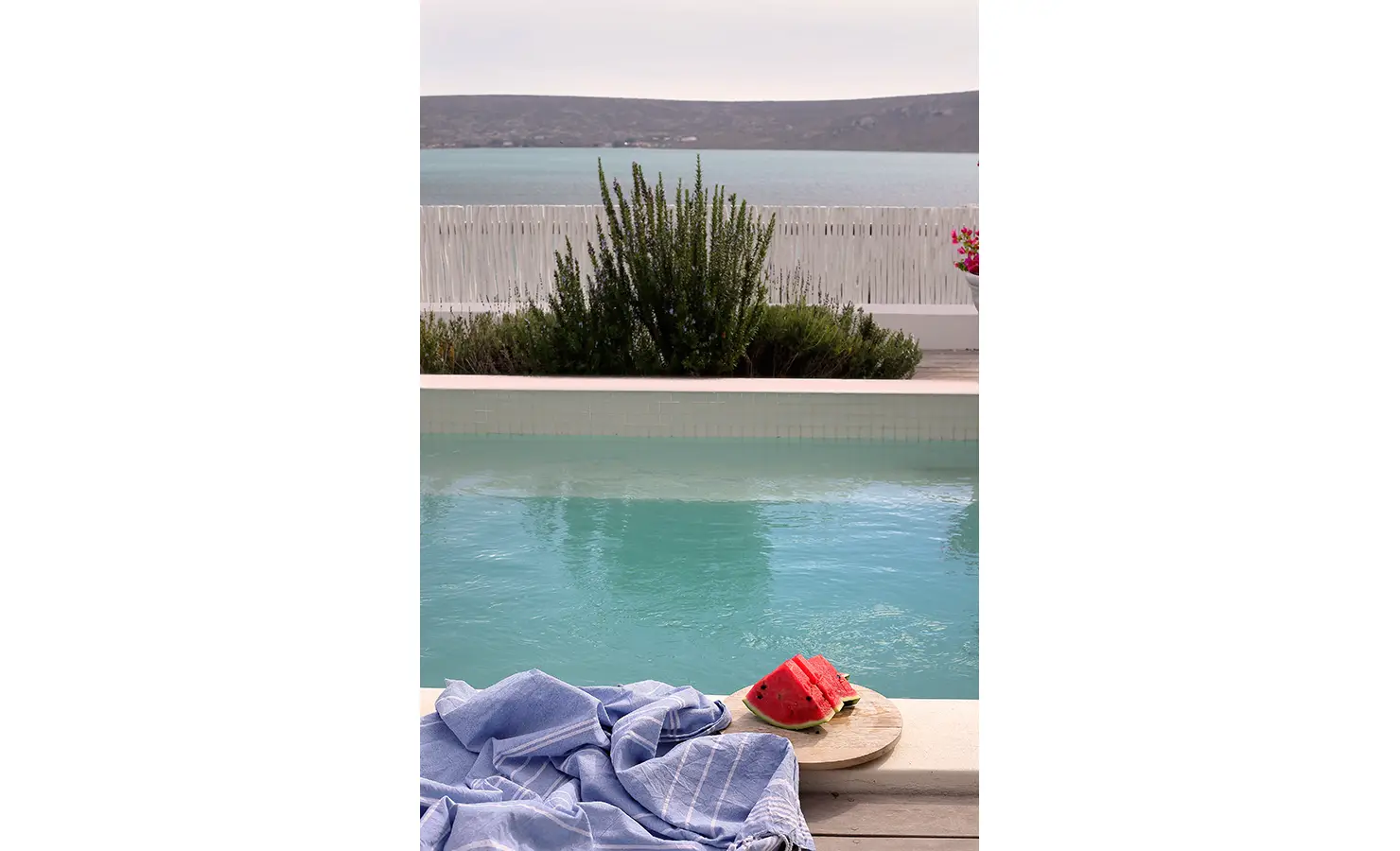 Perfect Hideaways: close-up of pool edge with blue towel and freshly cut watermelon against a calm lagoon, Langebaan, Lagoon Lookout.