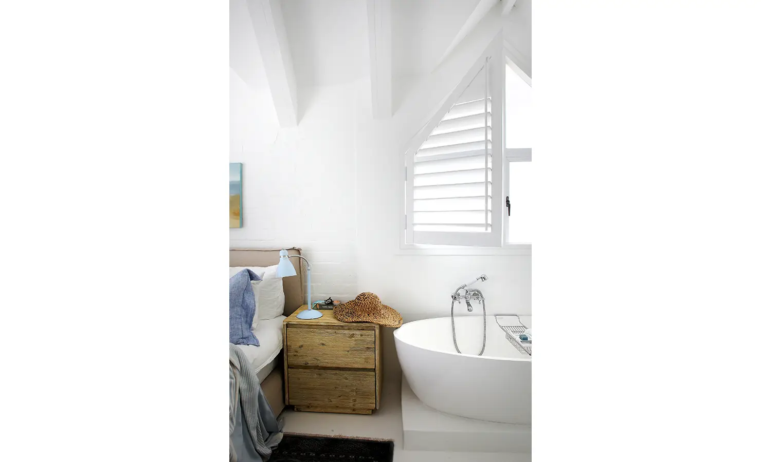 Perfect Hideaways: serene en-suite nook with a freestanding oval bath beneath a shuttered triangular window, rustic bedside and pale-blue lamp, Langebaan, Lagoon Lookout.
