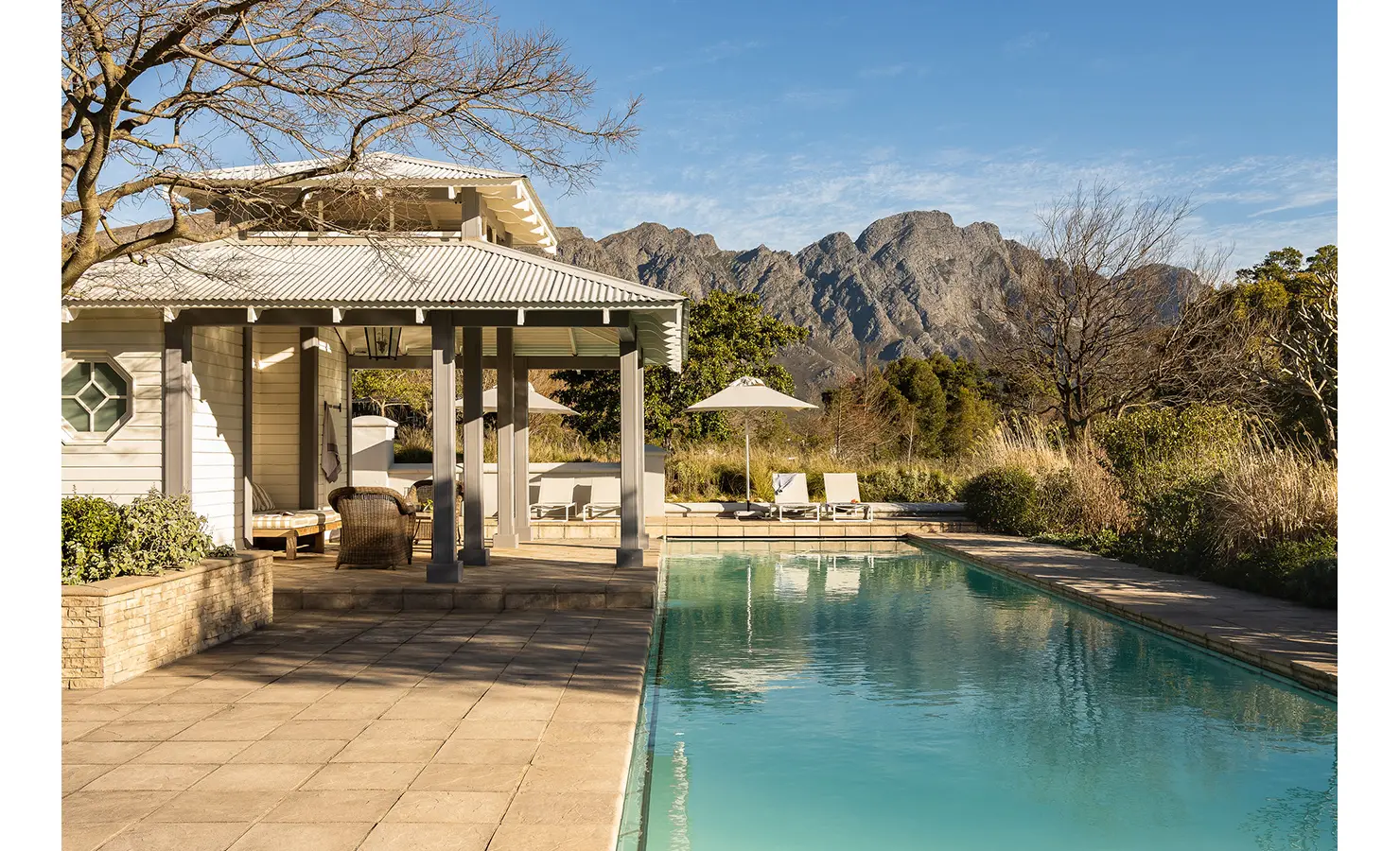 Perfect Hideaways tranquil poolside pavilion with sun loungers and mountain views surrounded by golden grasses and trees, Franschhoek, Varuna.