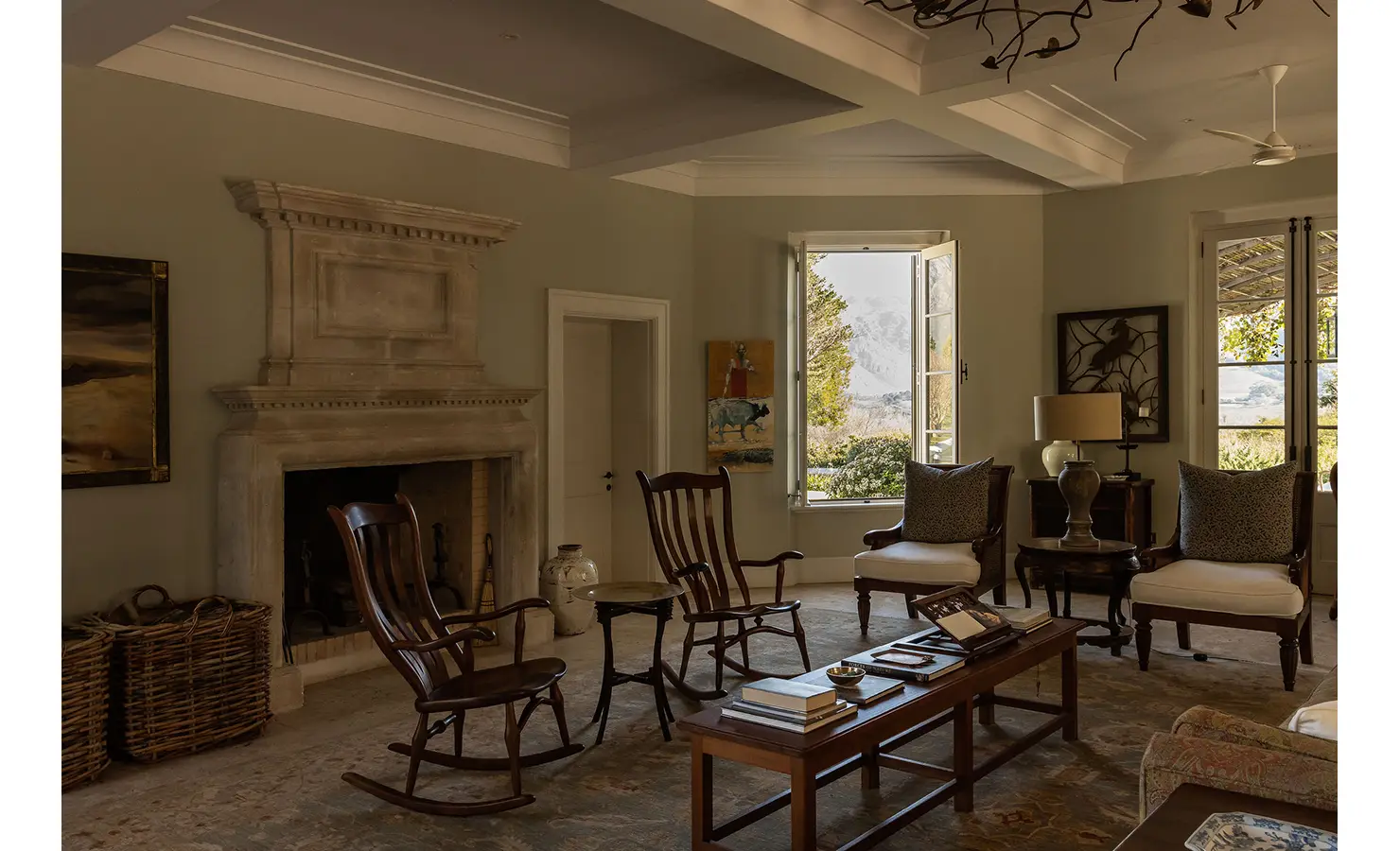Perfect Hideaways cozy lounge with an ornate stone fireplace, classic wooden rocking chairs, and mountain views through open windows, Franschhoek, Varuna.