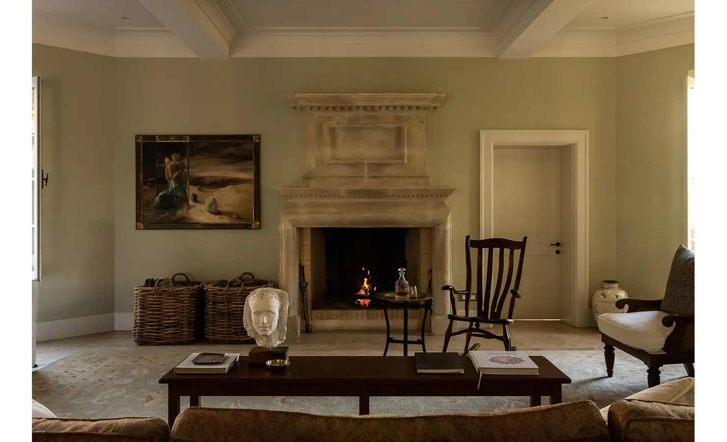 Perfect Hideaways warm and inviting sitting area centered around a lit stone fireplace, decorated with sculptures and woven baskets, Franschhoek, Varuna.