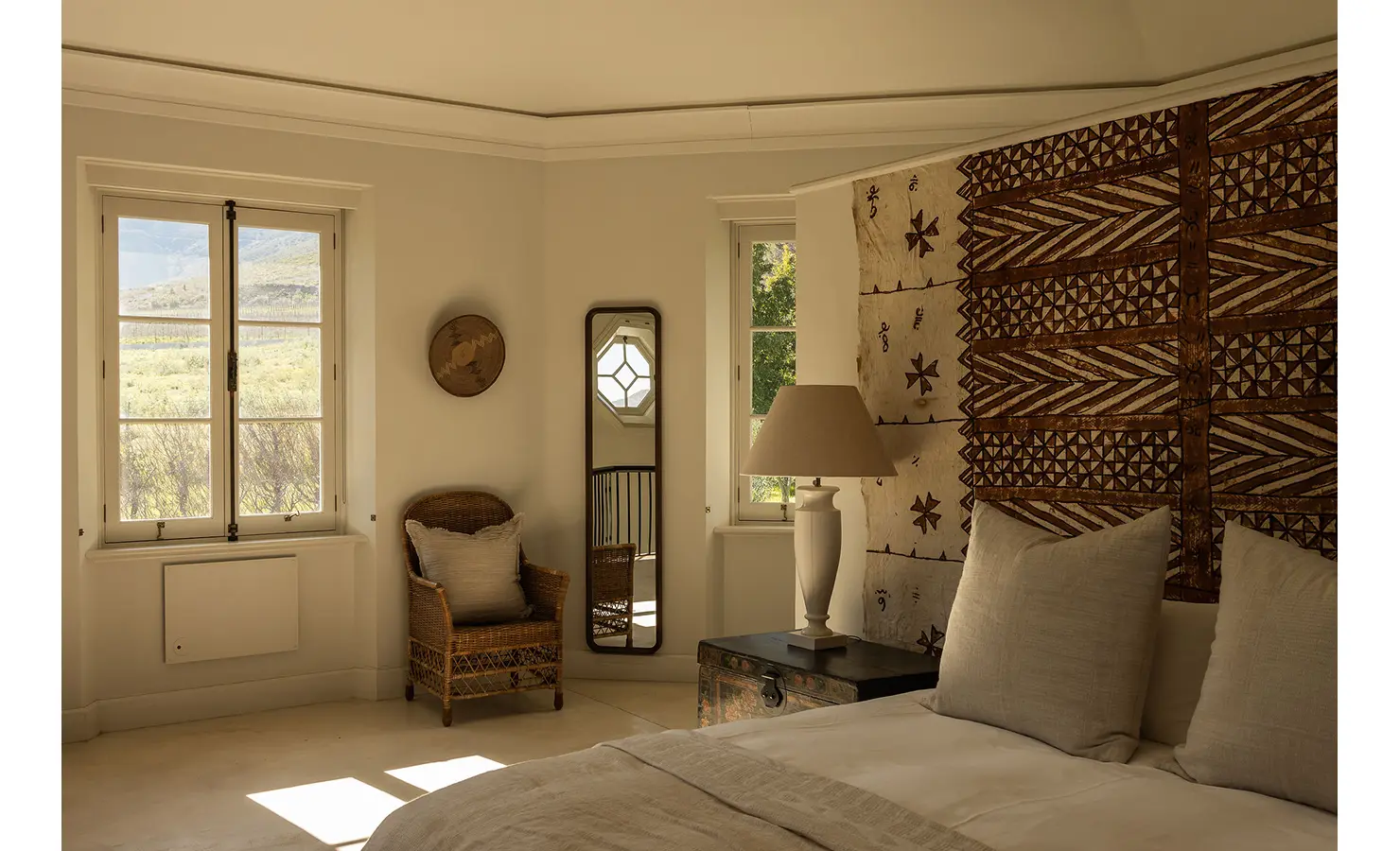 Perfect Hideaways minimalist bedroom with woven textures, natural tones, and a striking tribal wall hanging above the bed, Franschhoek, Varuna.