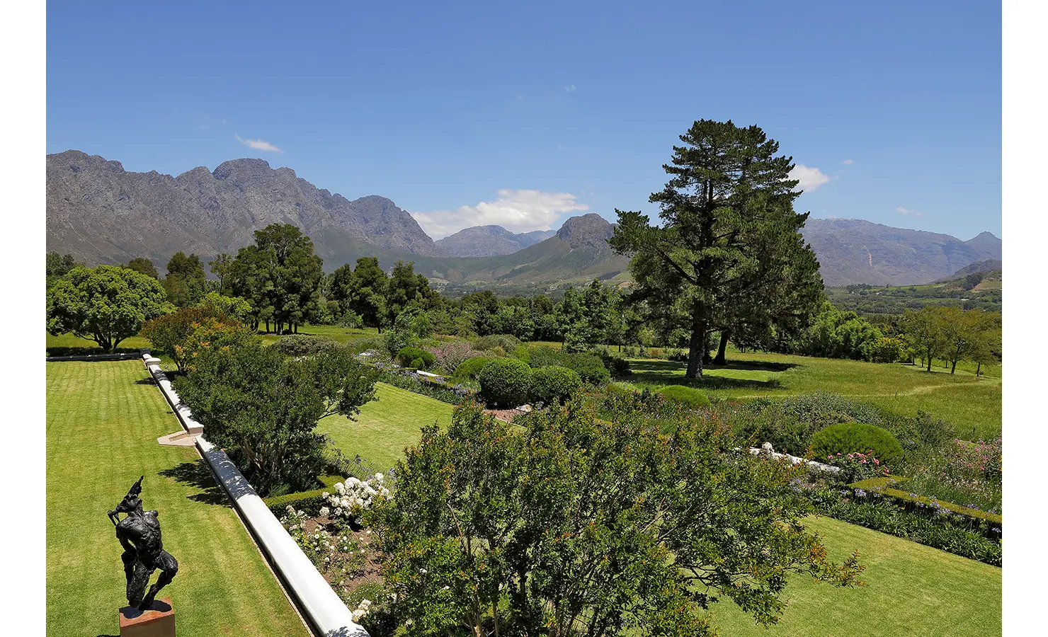 Perfect Hideaways sweeping garden view with manicured lawns, vibrant flower beds, sculptures, and mountains rising in the distance, Franschhoek, Varuna.