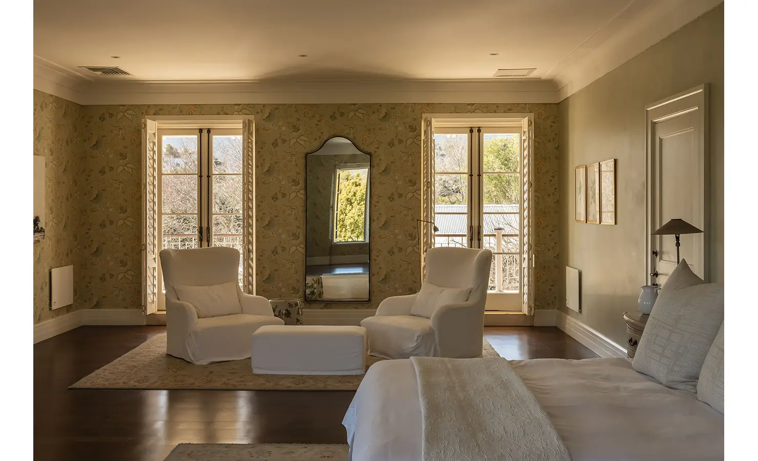 Perfect Hideaways spacious bedroom featuring floral wallpaper, soft neutral tones, and two white armchairs facing large sunlit windows, Franschhoek, Varuna.