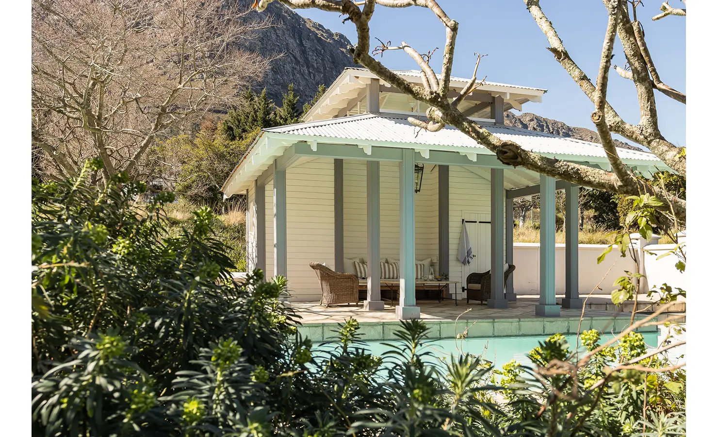 Perfect Hideaways charming poolside pavilion surrounded by greenery and mountain views, with wicker seating beneath a pale blue roof, Franschhoek, Varuna.