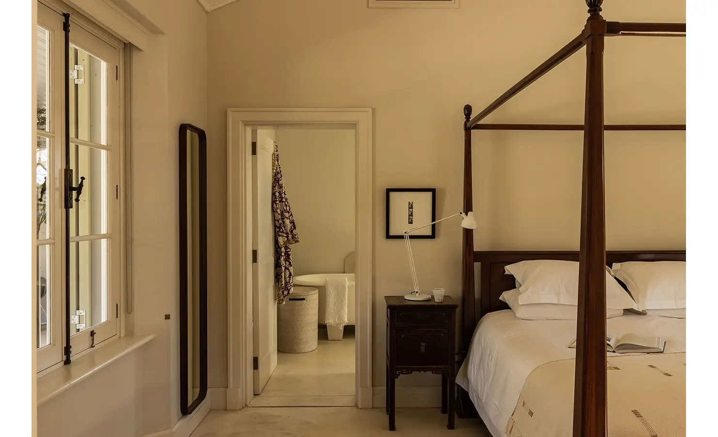 Perfect Hideaways elegant bedroom with a four-poster bed, bedside lamp, and adjoining bathroom visible through an open door, Franschhoek, Varuna.