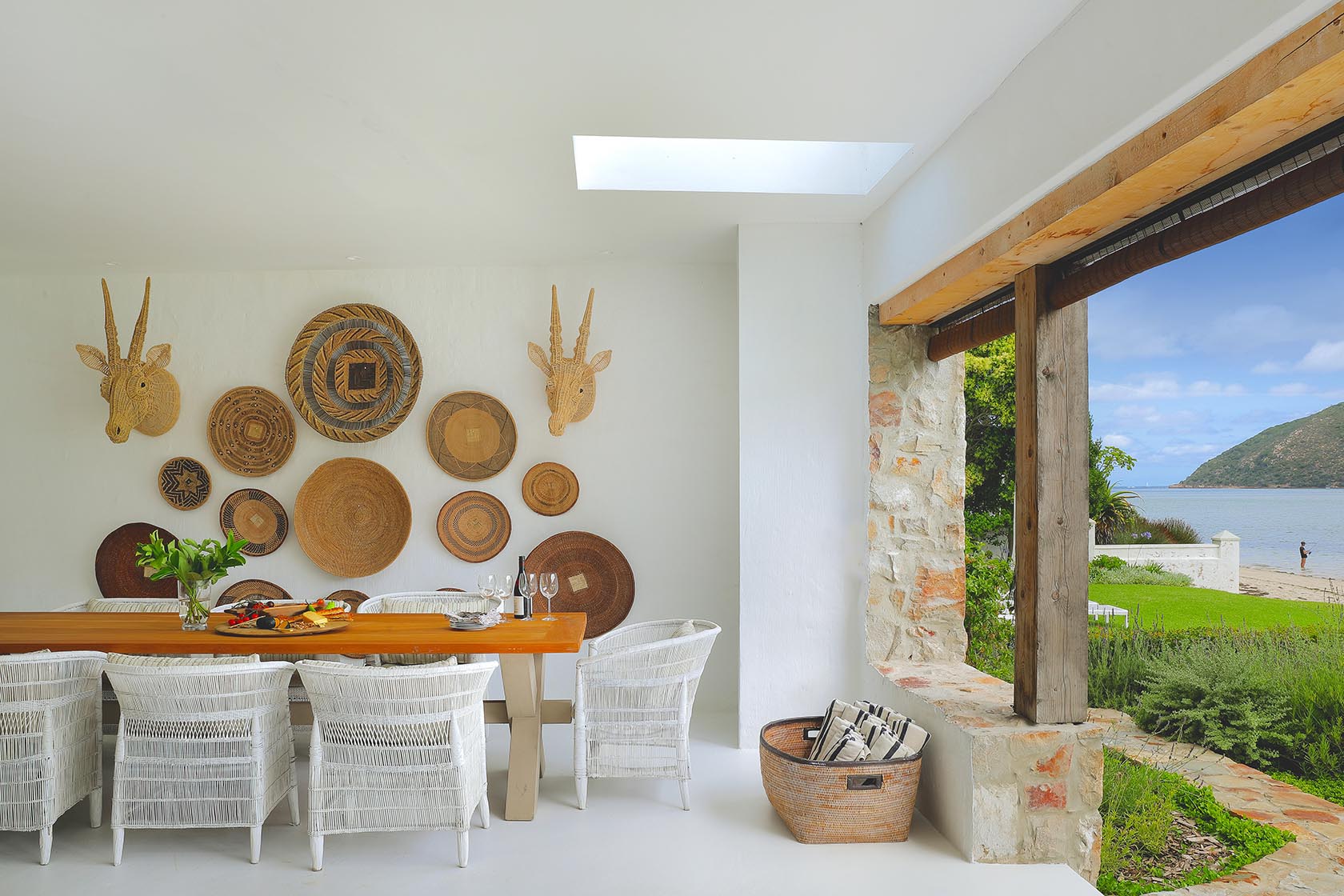 Perfect Hideaways: Light-filled dining space with white woven chairs and a basket wall, flowing out to the beach and lagoon, Knysna, Tides Reach