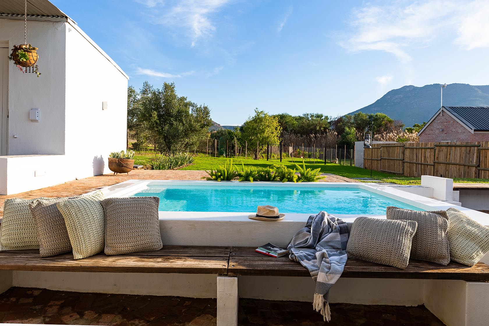 Perfect Hideaways-Outdoor plunge pool bordered by a built-in wooden bench with textured cushions, a straw hat and throw casually placed, overlooking a green garden and distant mountain views Valley Cottage, Riebeek Casteel, Western Cape, South Africa
