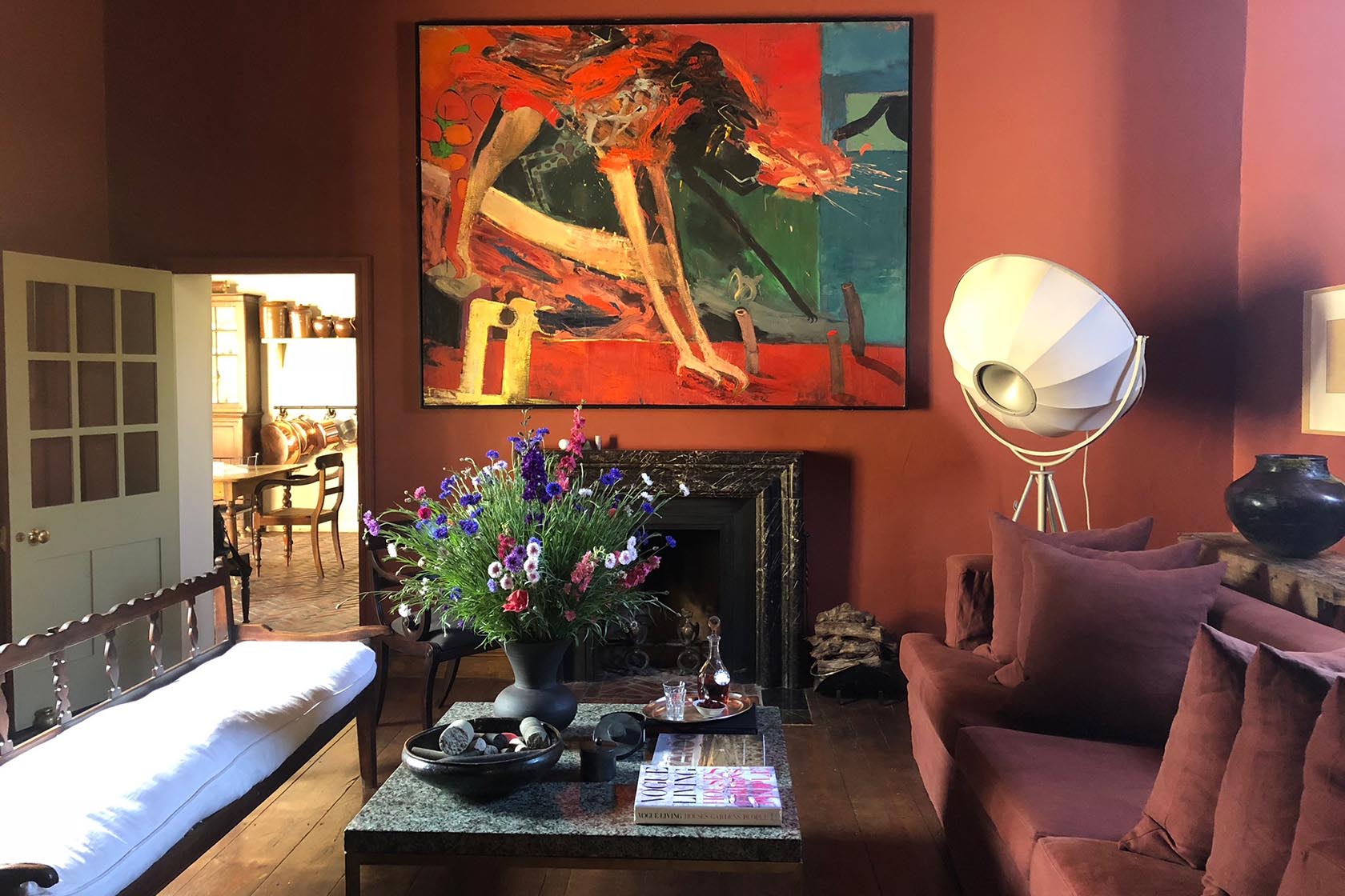 Perfect Hideaways- A warmly styled sitting room with terracotta walls, a large abstract painting above a dark fireplace, a low coffee table with books and flowers, a rust-coloured sofa, sculptural floor lamp and an open doorway leading to a dining space Jonkmanshof, Montague, Western Cape, South Africa
