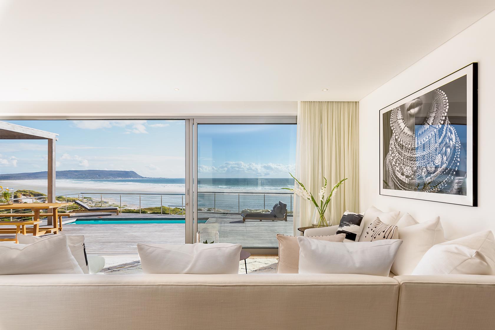 Perfect Hideaways - Elegant living room with sliding glass doors opening onto a sea-facing deck, showcasing pool, loungers and sweeping Noordhoek ocean views Noordhoek Seashore_Noordhoek_Southern Peninsula_Cape Town_Western Cape_South Africa