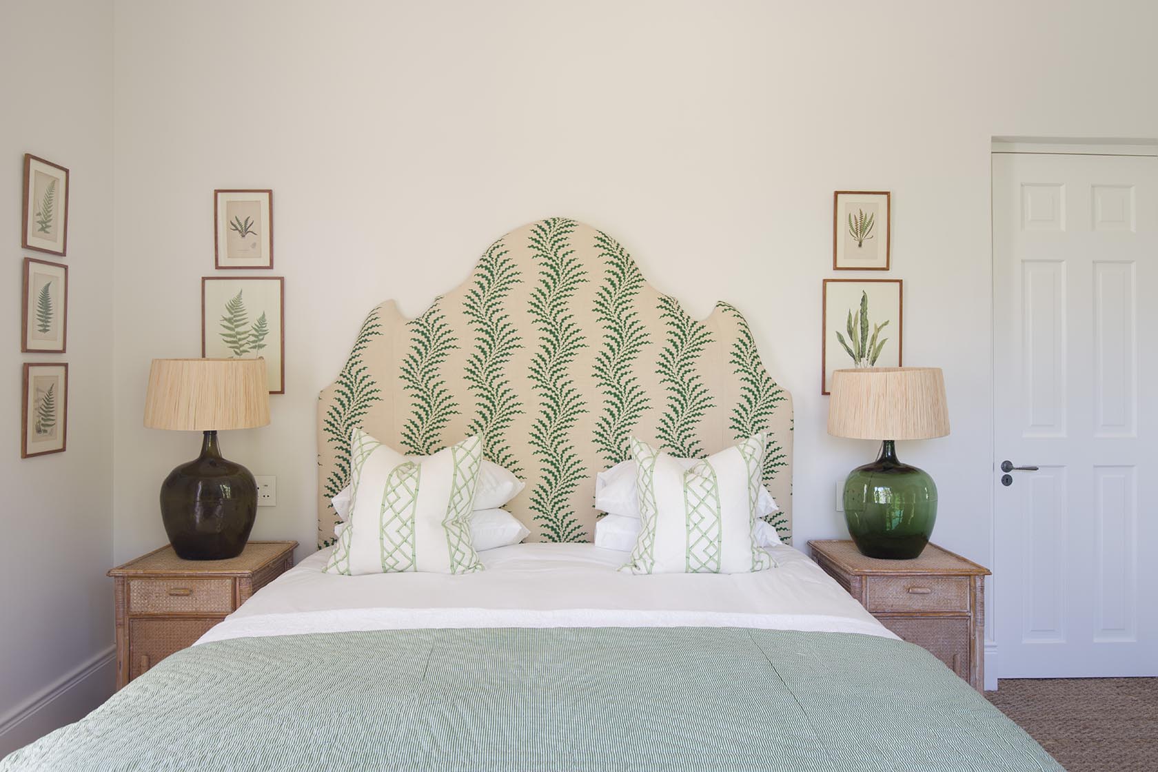 Perfect Hideaways – A serene bedroom with a soft green patterned headboard, botanical artwork on the walls, matching bedside lamps with large green bases, and a neatly made bed with white linens and pale green accents, creating a calm, nature-inspired atmosphere. La Cotte Orchard Cottages, Franschhoek South Africa