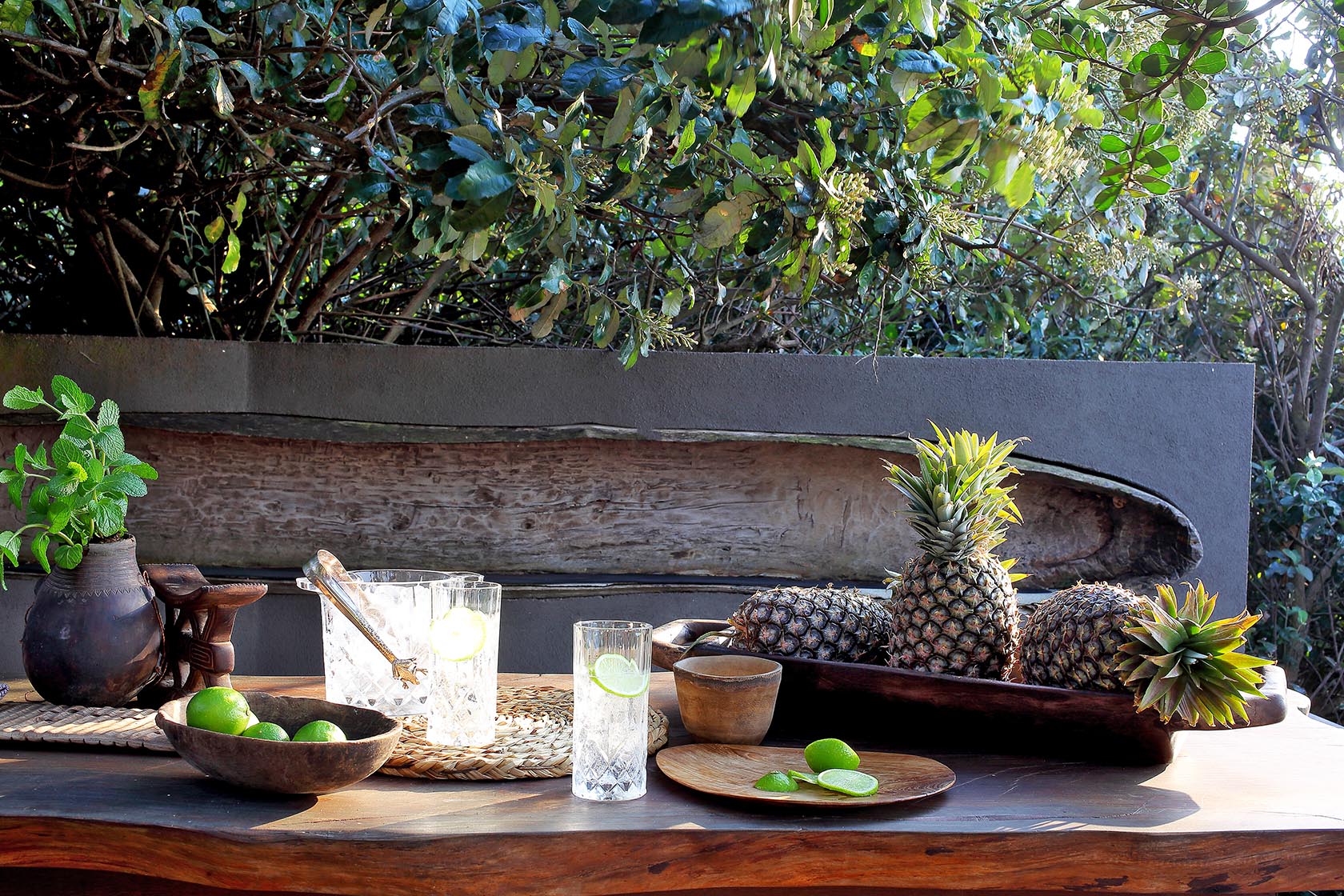 Perfect Hideaways- A rustic outdoor drinks setting with fresh pineapples, limes, glassware, and wooden serving pieces arranged on a table surrounded by leafy greenery cowrie Cottage, Dolphin Coast, Kwazulu- Natal, South Africa