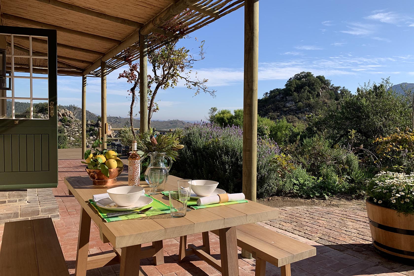 An outdoor dining table set under a shaded veranda, surrounded by lavender and fynbos, with far-reaching views of the surrounding hills. Francois Cottage, Franschhoek