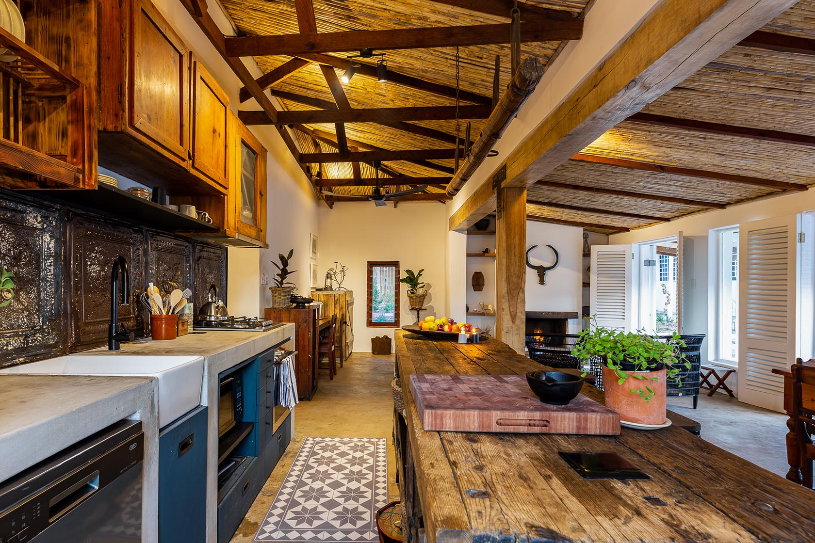 Perfect Hideaways-Rustic open-plan kitchen with a long wooden island, concrete countertops, vintage cabinetry, and exposed timber beams beneath a reed ceiling, styled with plants and tableware Valley Cottage, Riebeek Casteel, Western Cape, South Africa