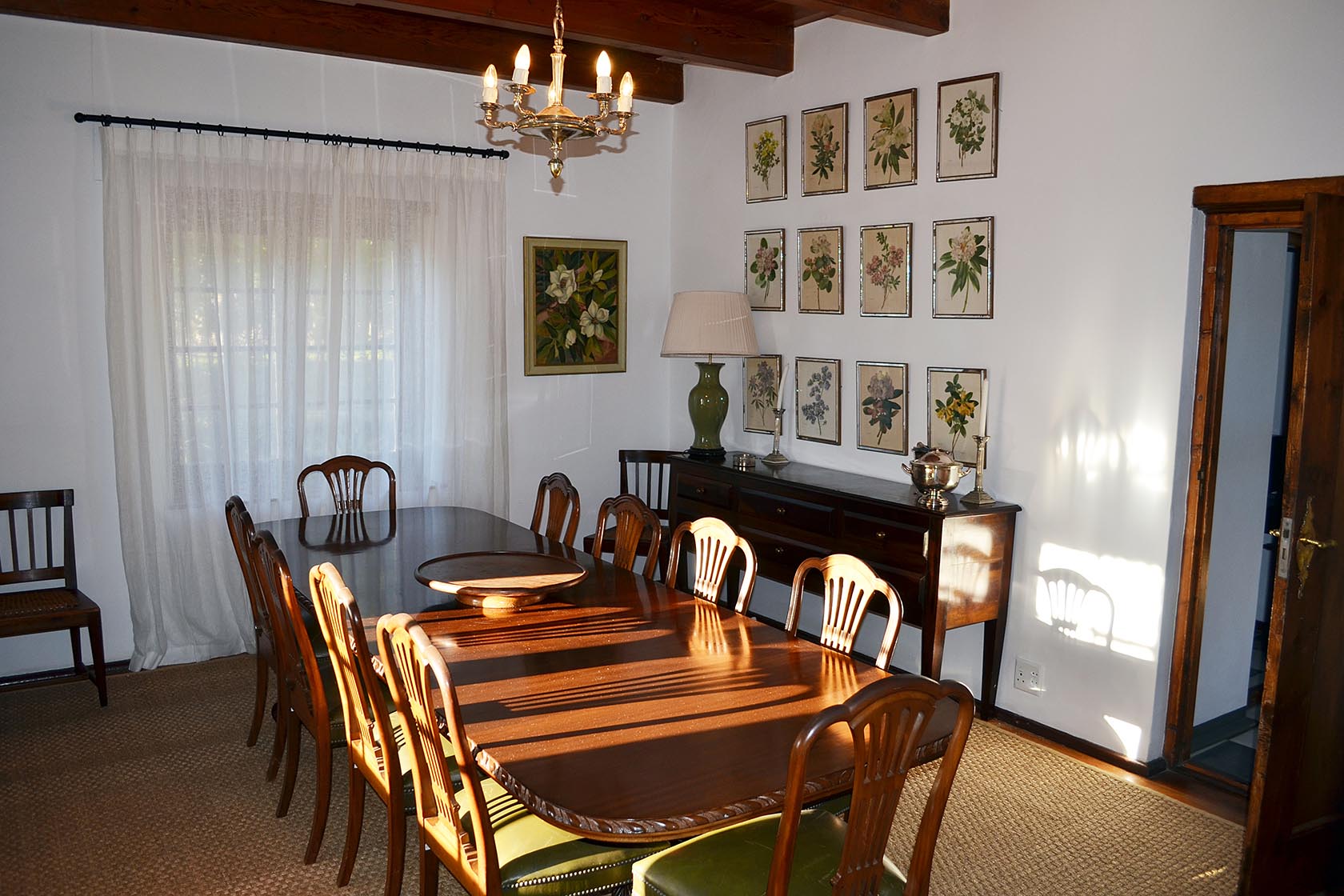 Perfect Hideaways – A formal dining room featuring a long polished wooden table, classic wooden chairs, botanical artwork on the wall, and soft natural light filtering through sheer curtains – Cottage 1685, Franschhoek, Western Cape, South Africa