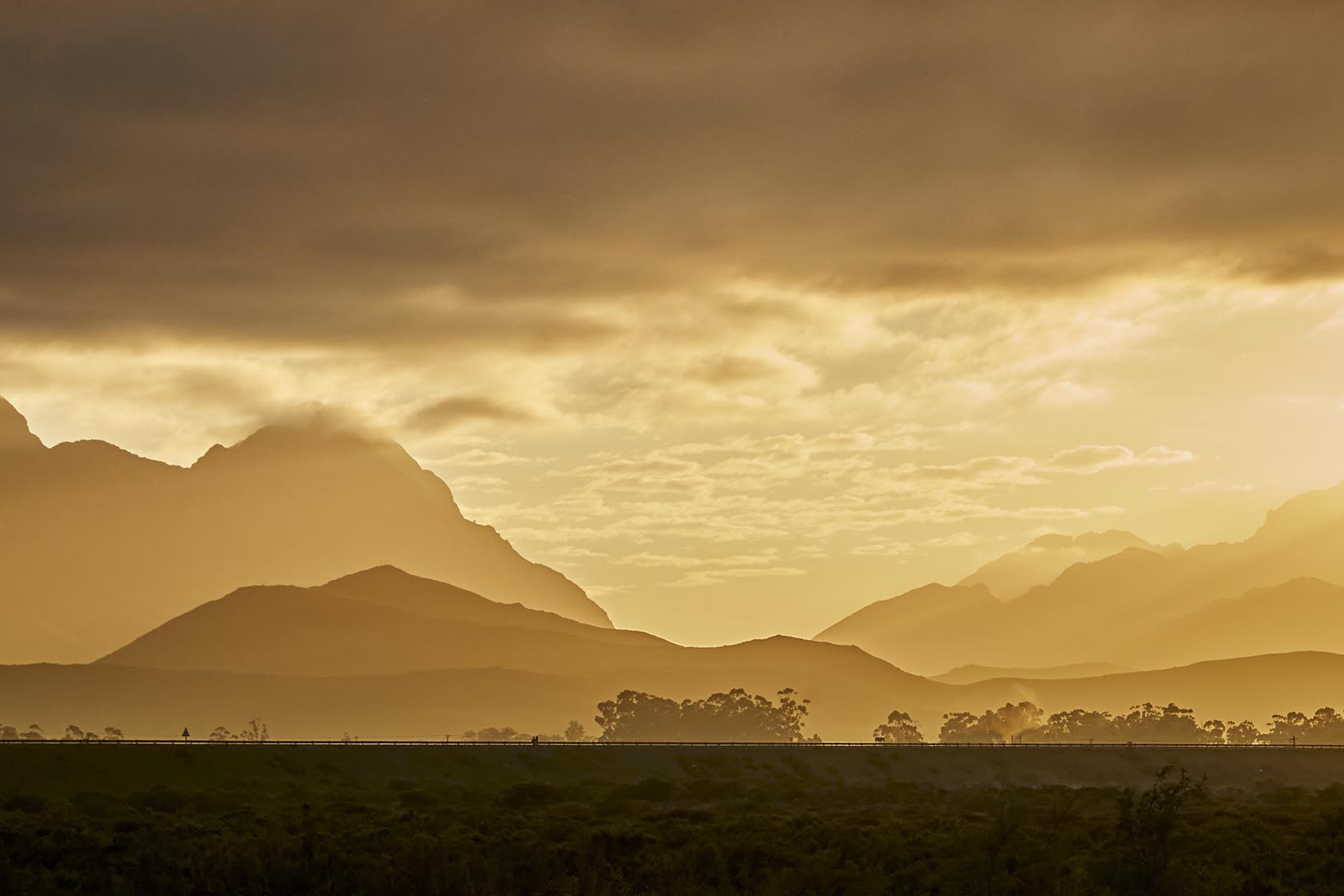 Perfect Hideaways - Layers of mountain ridges glowing in warm golden light beneath a dramatic cloudy sky, creating a peaceful early-morning valley scene High Country Cottage_Wolseley_Cape Winelands_Western Cape_South Africa