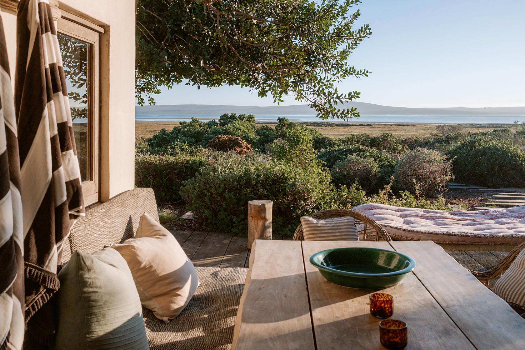 Perfect Hideaways- Outdoor deck dining table with a ceramic bowl, candles and cushioned seating overlooking lush fynbos and expansive lagoon views in soft afternoon light, Yellowwood Cottage, Churchhaven, Western Cape, South Africa
