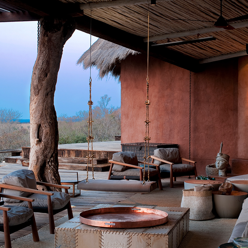 Perfect Hideaways - An aerial view of a sculptural, thatched-roof safari lodge set on a rocky escarpment surrounded by dense green bushveld, featuring organic architecture, tall brick chimneys, curved structures, expansive wooden decks, and a cliffside swimming pool overlooking the wilderness – The Observatory, Leobo Private Nature Reserve, Limpopo South Africa