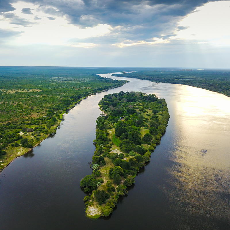 Perfect Hideaways: Aerial image of Zambezi river, surrounded by lush vegetation under a cloudy blue sky. Chundu Island, Zambezi National Park.