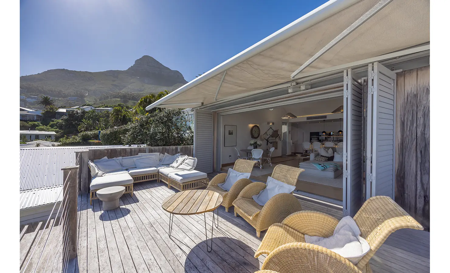 Perfect Hideaways Expansive mountain-view deck with wicker loungers, round wooden tables, and soft cushioned seating flowing seamlessly into an open-plan living and dining area through wide folding doors beneath a large retractable awning Clifton, Luna del Mar.