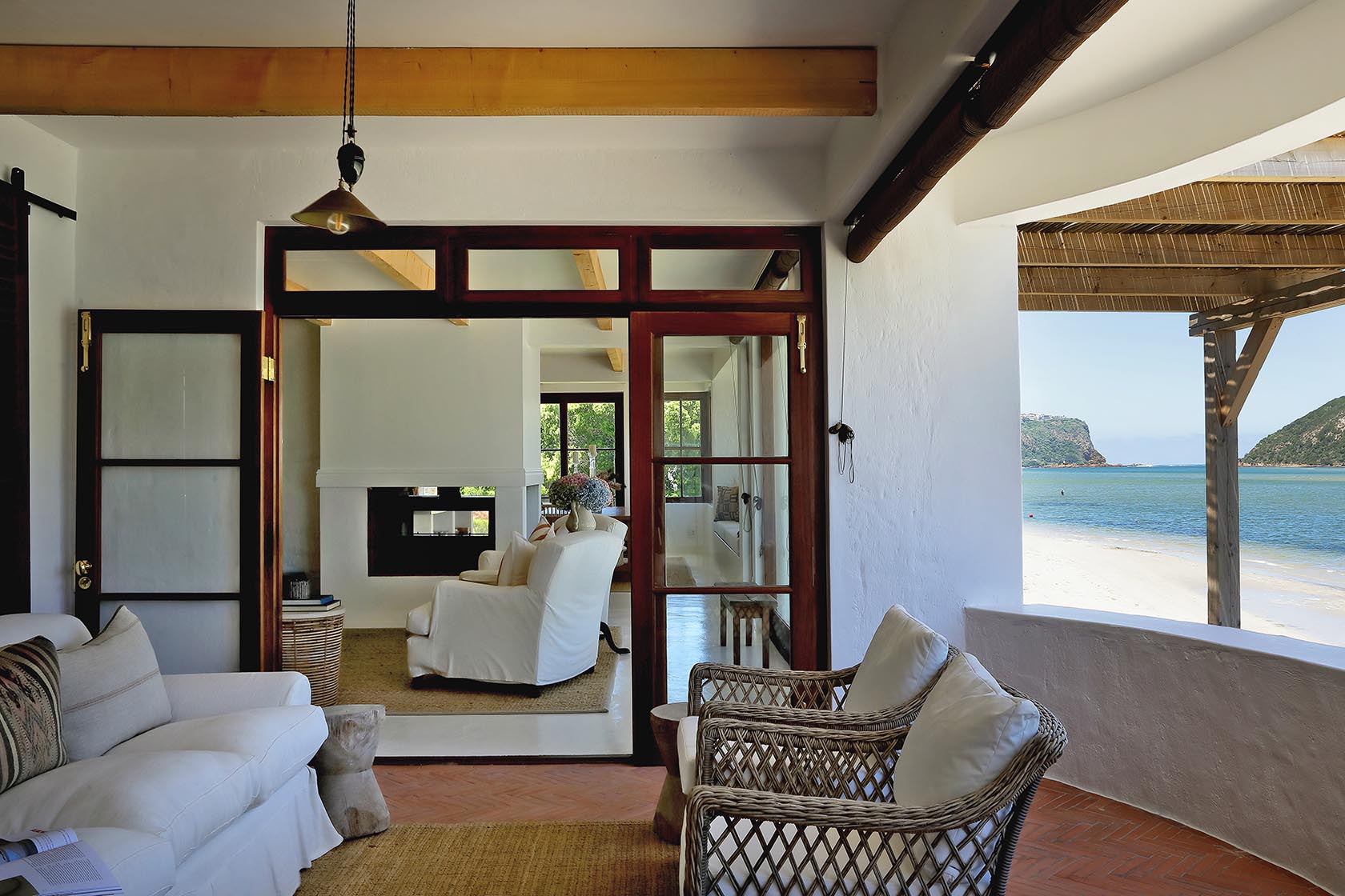 Perfect Hideaways: Cosy sitting room with wicker chairs and white sofa opening to the beach through timber-framed doors, Knysna, Tides Reach