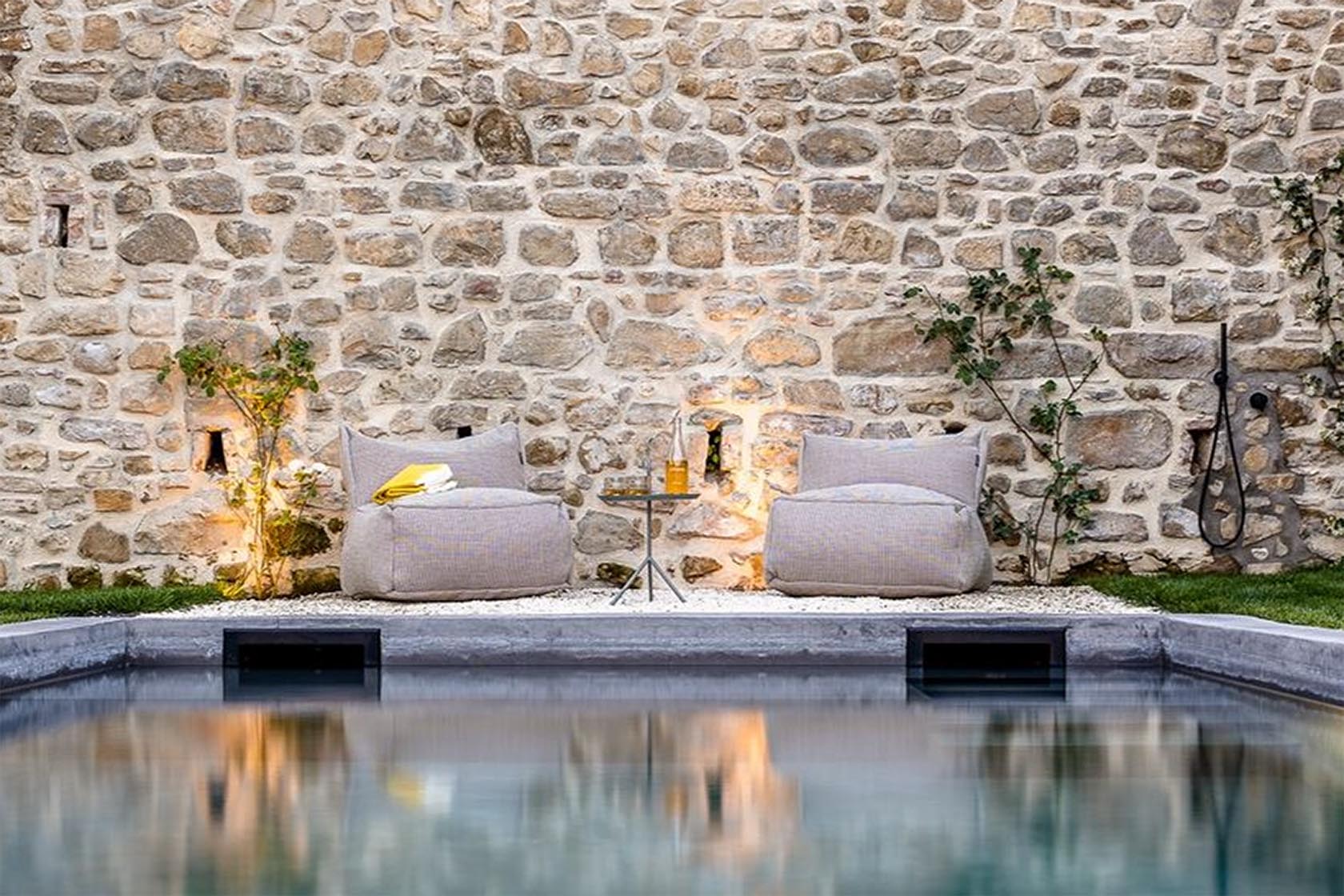 Perfect Hideaways tranquil poolside seating against a rustic stone wall at dusk, Umbria Cottage, Collazzone