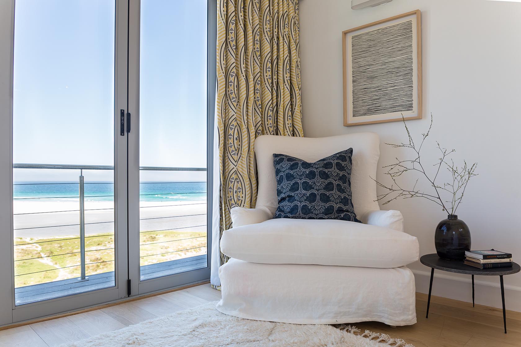 Perfect Hideaways - Cozy bedroom reading nook with upholstered armchair, patterned curtains and floor-to-ceiling glass doors overlooking Noordhoek beach Noordhoek Seashore_Noordhoek_Southern Peninsula_Cape Town_Western Cape_South Africa