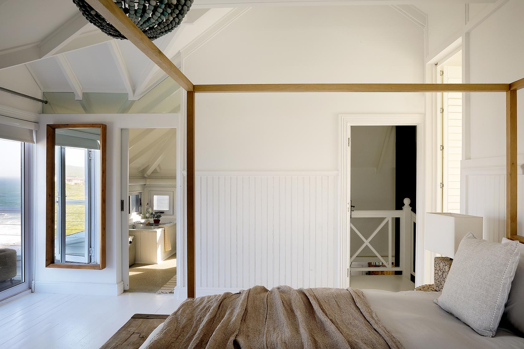 Perfect Hideaways - Calm bedroom interior with a four-poster bed, white panelled walls and exposed beams, opening toward an en-suite bathroom and balcony beyond Cape Cottage_Yzerfontein_West Coast_Western Cape_South Africa
