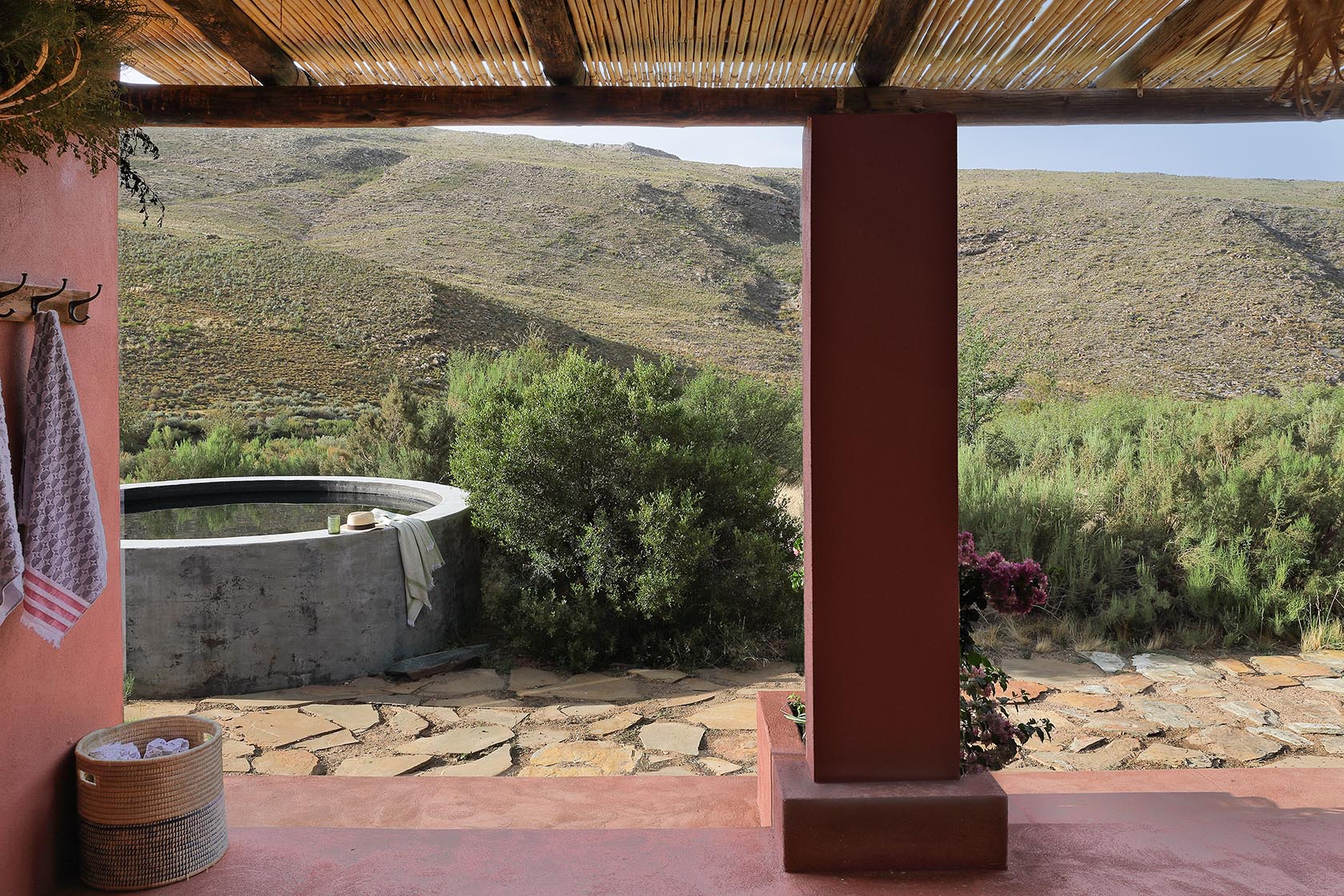 Perfect Hideaways – A covered veranda with bamboo roofing overlooks a circular plunge pool set among dense Karoo shrubs. Towels hang from rustic hooks, and light filters gently through the pergola. Sheperd's Cottage, Prince Albert