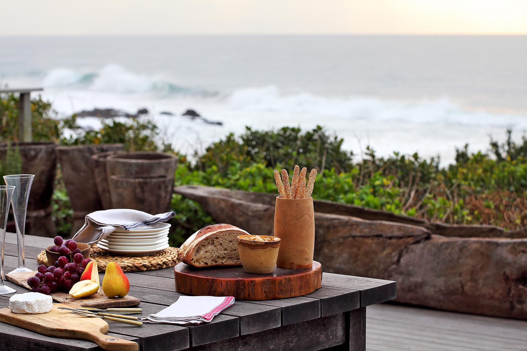 Perfect Hideaways- An outdoor dining setup with artisan bread, fruit, tableware, and wooden serving boards arranged on a deck overlooking the ocean cowrie Cottage, Dolphin Coast, Kwazulu- Natal, South Africa