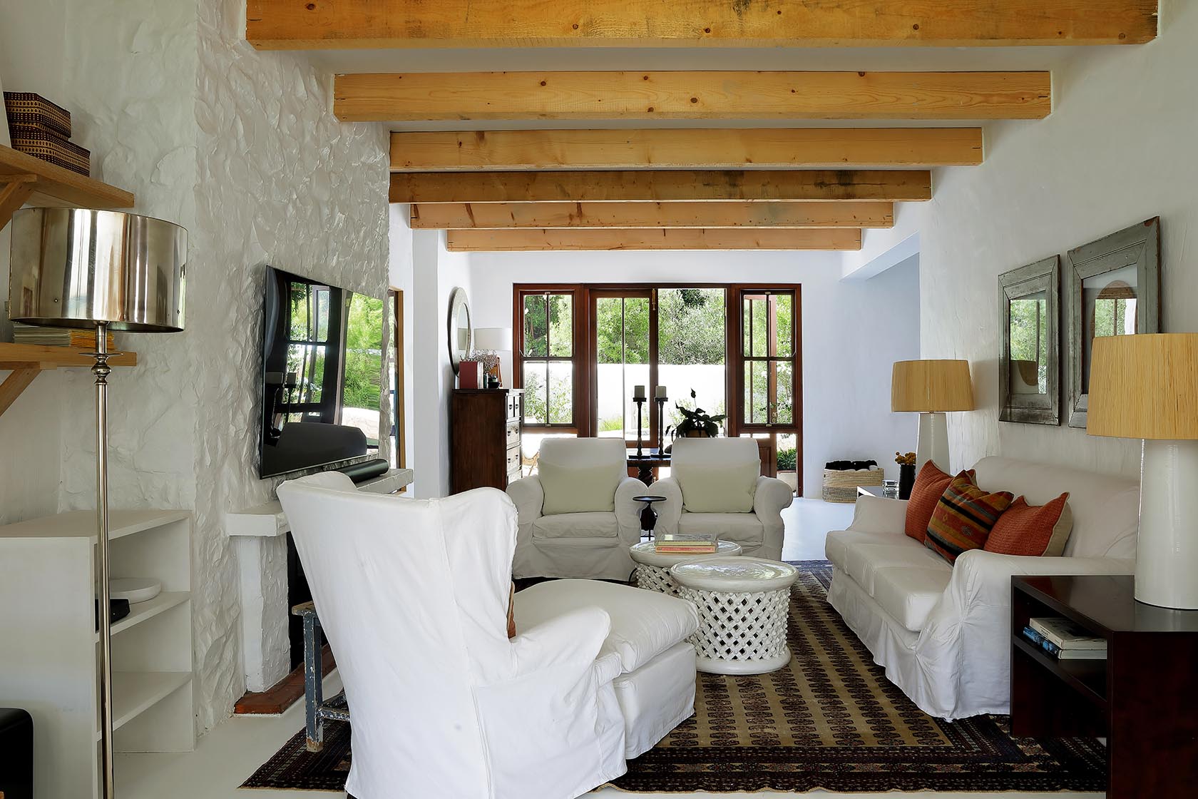 Perfect Hideaways: Art-filled living area with round wooden table, layered rugs and beams opening towards the water, Knysna, Tides Reach