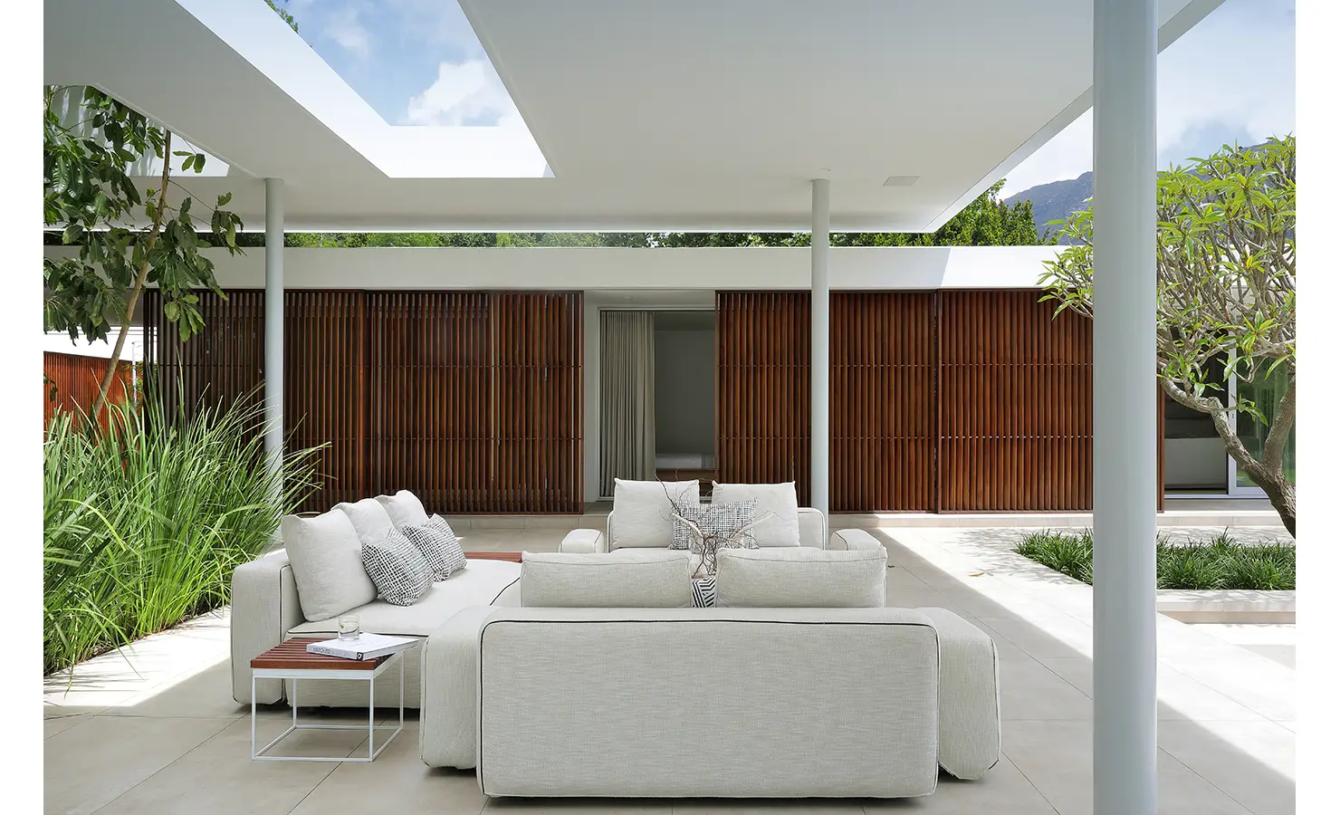 Perfect Hideaways A serene covered patio featuring soft cream sofas beneath a sleek white skylight structure, bordered by tall grasses and warm wooden slatted walls Pure Living, Bishopscourt