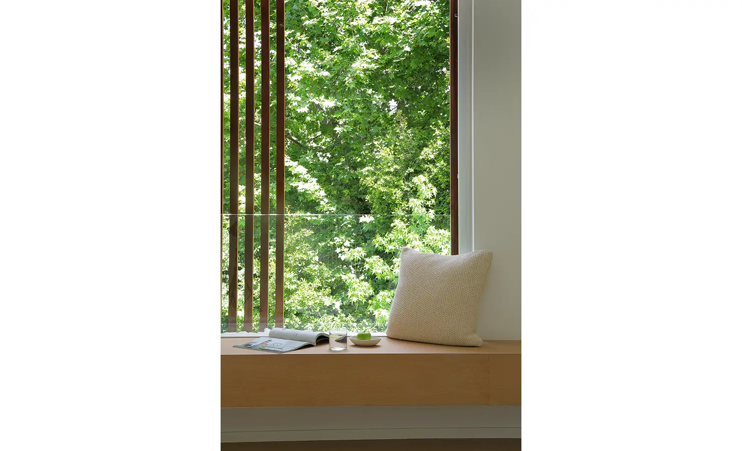 Perfect Hideaways A peaceful window-seat nook with a cushioned bench, open magazine, and small glass of water, overlooking vibrant green foliage framed by vertical wooden slats Pure Living, Bishopscourt