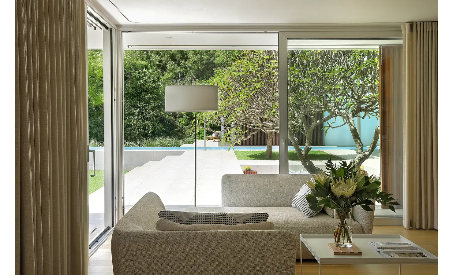 Perfect Hideaways A bright living area opening to the terrace, centered on a sculptural flowering tree outside, with soft neutral seating and a clear view of the pool Pure Living, Bishopscourt