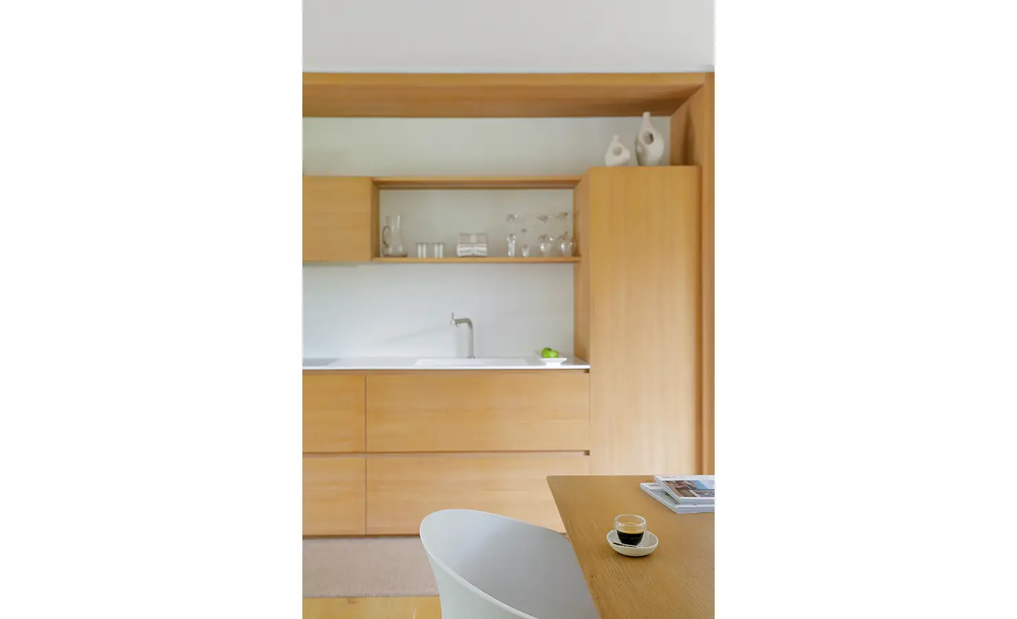 Perfect Hideaways A minimalist light-wood kitchenette with clean lines, open shelving, simple ceramics, and a small espresso set on the dining table Pure Living, Bishopscourt