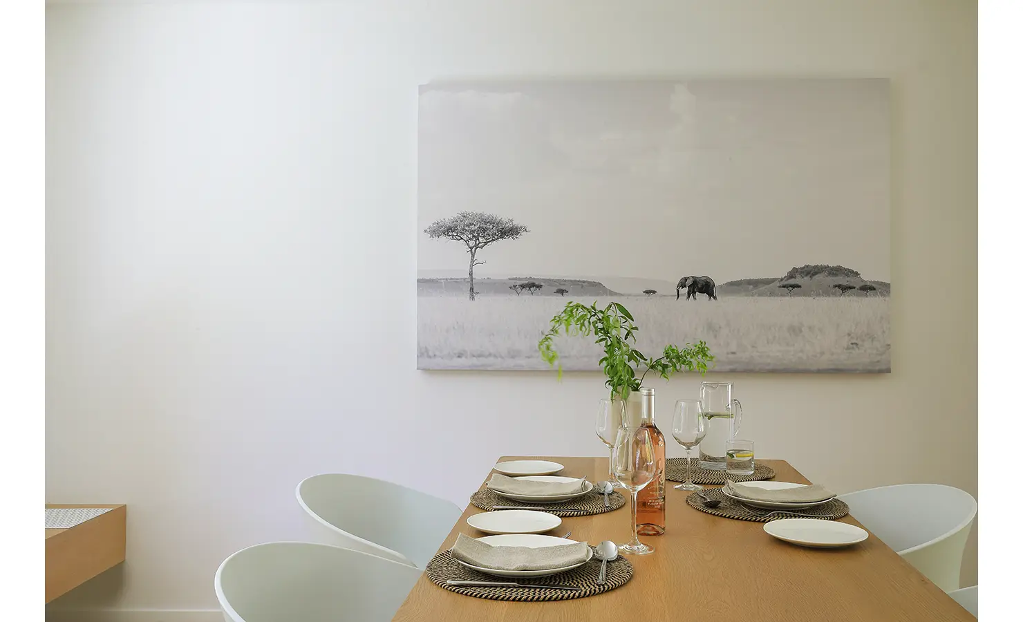 Perfect Hideaways A beautifully set dining table with neutral plates and glassware sits beneath a large monochrome artwork of an African landscape featuring acacia trees and elephants Pure Living, Bishopscourt
