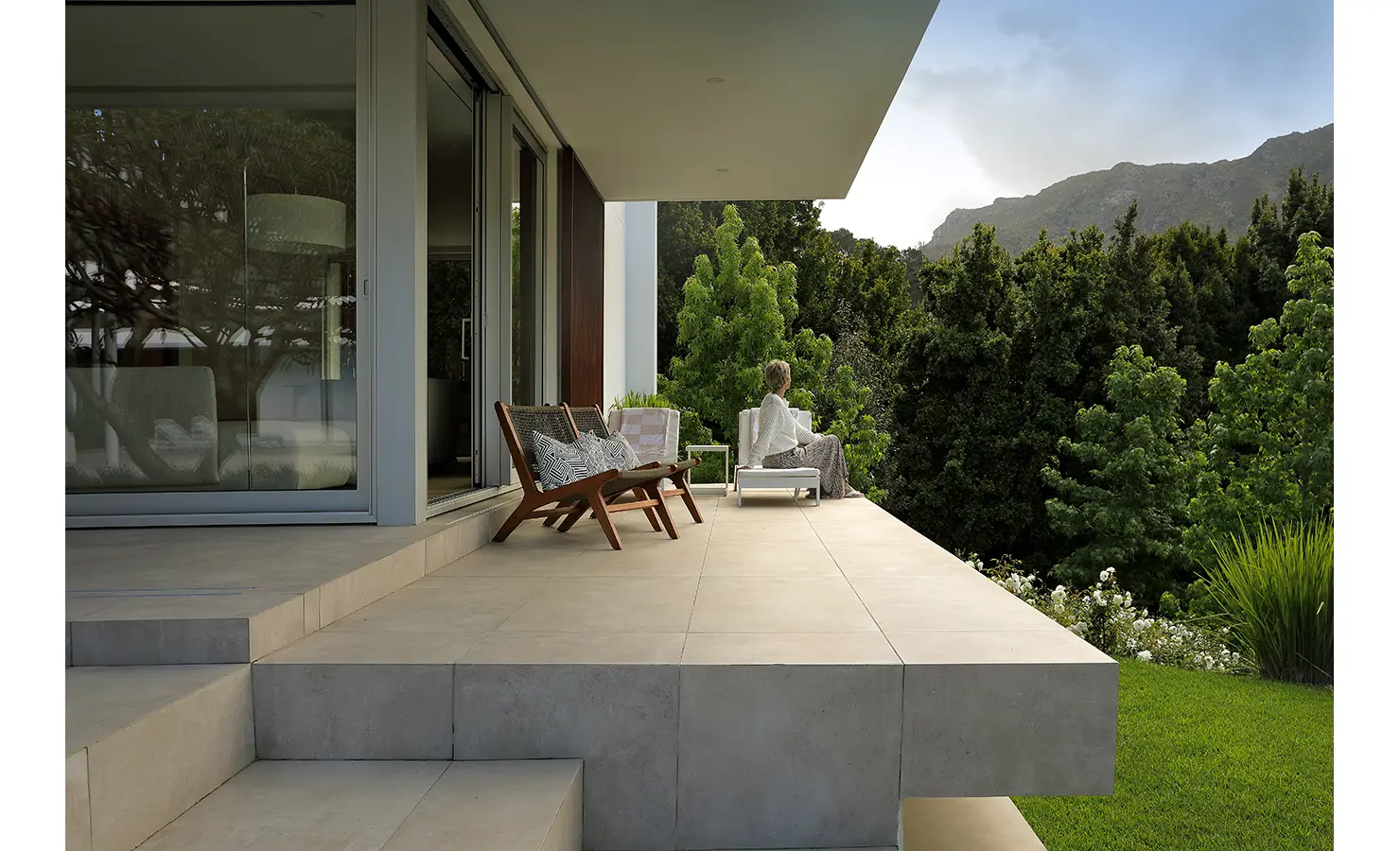 Perfect Hideaways A peaceful terrace where a woman relaxes on a lounger, surrounded by textured greenery and views of the mountains in soft evening light Pure Living, Bishopscourt