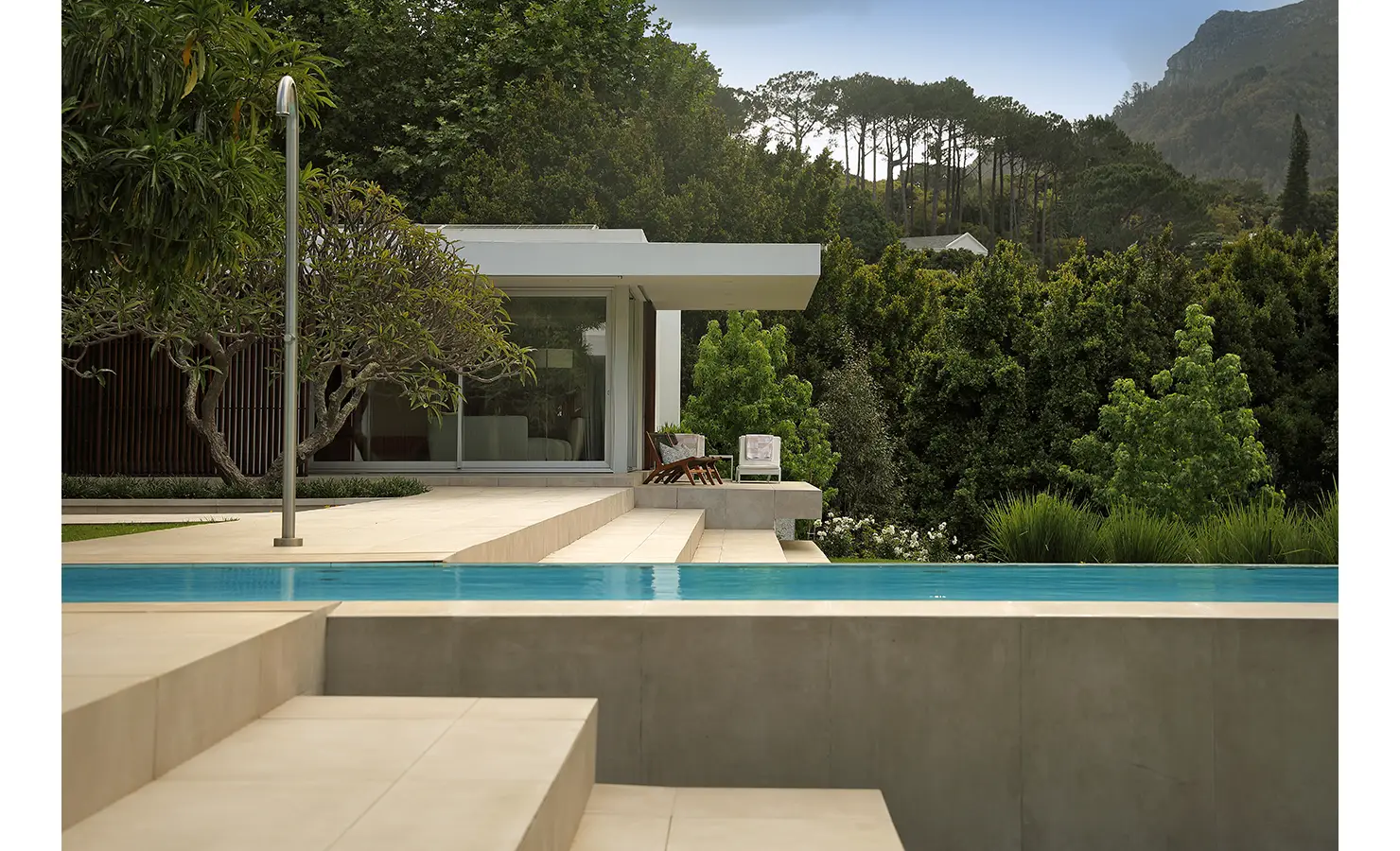 Perfect Hideaways A sleek modern pool stretches toward a pavilion framed by tall trees and sculptural greenery, creating a serene retreat Pure Living, Bishopscourt