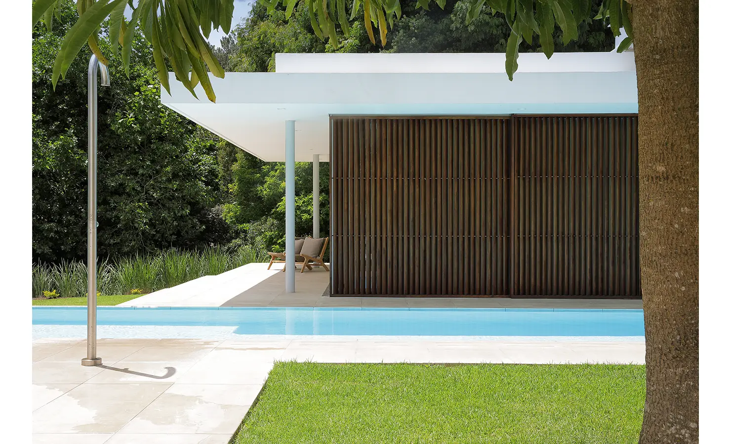 Perfect Hideaways A minimalist outdoor pavilion with timber screens stands beside a turquoise pool and lush green lawn Pure Living, Bishopscourt